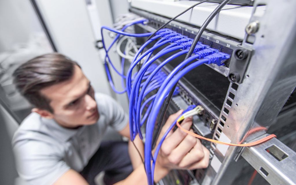 Young man working in network server room with fiber optic hub for digital communications and internet