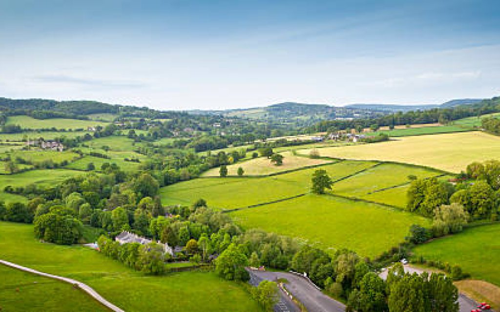Dramatic aerial view of gently rolling patchwork farmland with pretty wooded boundaries, in the beautiful surroundings of the Cotswolds, England, UK. Stitched panoramic image.
