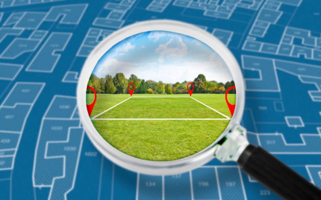 Land management with an imaginary cadastral map of territory with a vacant land available for sale or building construction - Concept seen through a magnifying glass