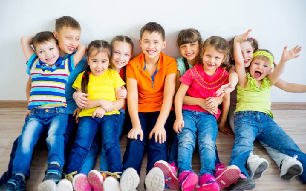 Several kids are sitting on floor in multicolored tshirts smiling