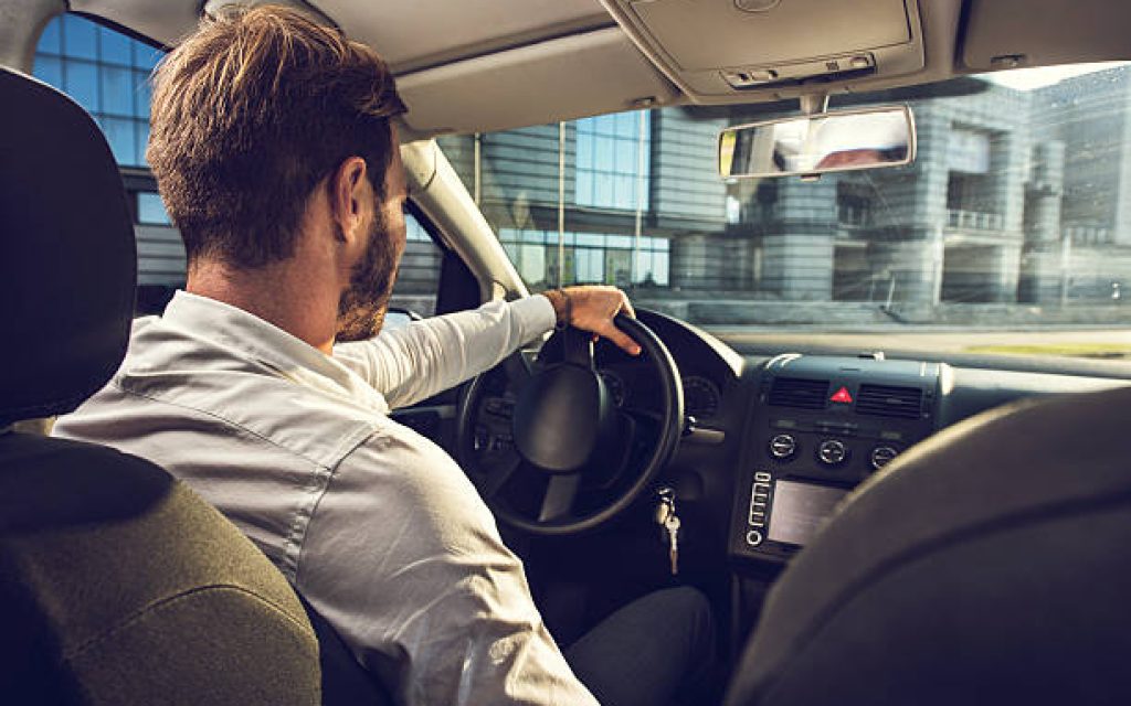 Businessman driving a car on his way to work. The photo is taken from the back seat.